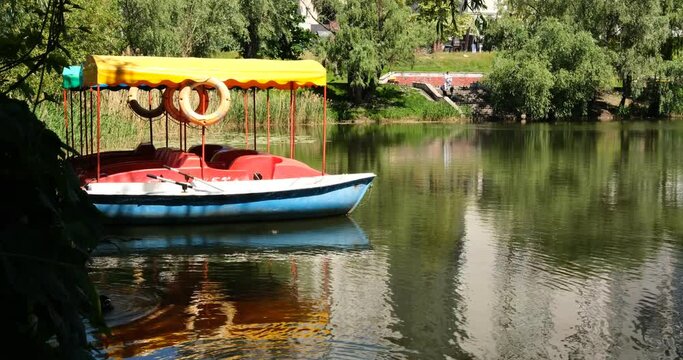 Boats and catamarans drift gently on serene lake waters near pier with reedy shore. Calm blue and white boats glide peacefully with slight ripples. Scenic lake view with tranquil boat movement.