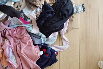 Clothes pile next to laundry basket filled with garments, on hardwood floor