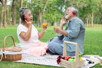 senior couple have a picnic wearing headphone to listen a music and holding orange juice glass in...