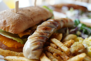 Sandwich with grilled sausages and french fries on wooden table