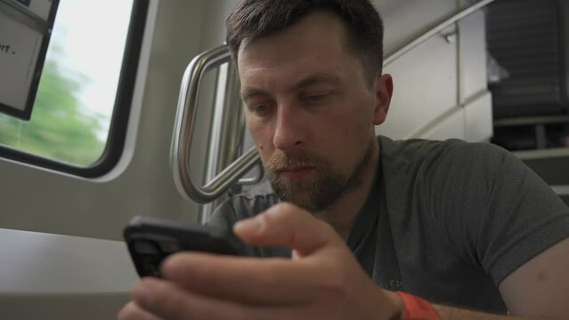 Young man travels on double decker train and sits on flyer using his smartphone. No available seating during railroad trip. Male commutes in dual deck train seated on flyer and surfing internet. 