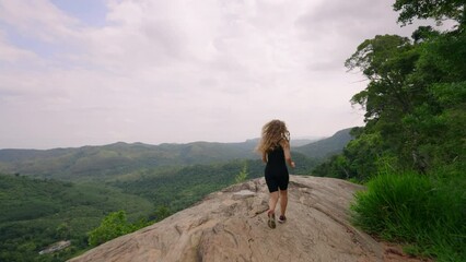 Woman in black hikes up mountain, embraces vast green panorama. Arms wide, she feels pure freedom, joy atop nature peak. Solo traveler explores, enjoys refreshing landscape, wilderness serenity. Slomo