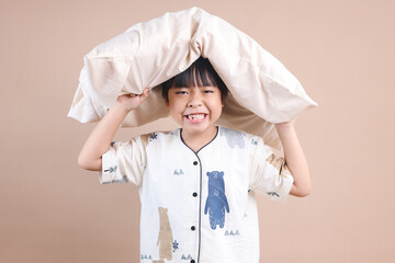 Kid Boy in Pajamas Holding Pillow Above The Head Against Beige Background