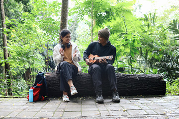 Young man playing guitar and sitting with his partner in nature