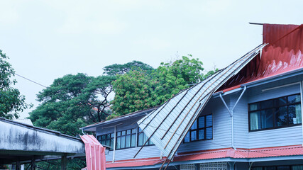Broken roof after a storm. The roof of a wooden building covered with metal sheets is broken and...