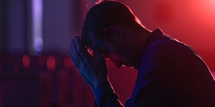 man is sitting down and holding his hands together to his face while he is praying
