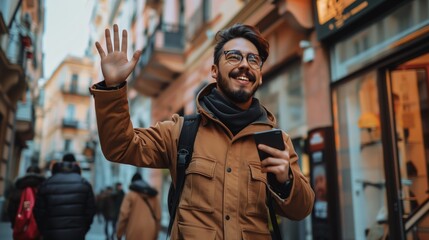 A happy trendy guy waving to a friend and holding cellphone on a street. 