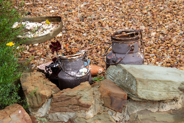 Two old rusted milk cans next to a rough stone wall image in horizontal format