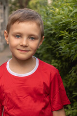 Close-up portrait of a smiling happy boy 7-8 years old in a red T-shirt in the park in summer