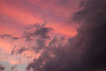A stormy dramatic sky is filled with clouds that are bathed in hues of pink and purple from the setting sun. Contrasting colors create a moody and atmospheric scene with dark, ominous cloud formations