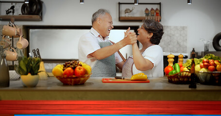 Indian Asian happy retired older senior couple pair hold hand dancing modern kitchen make fun joy...