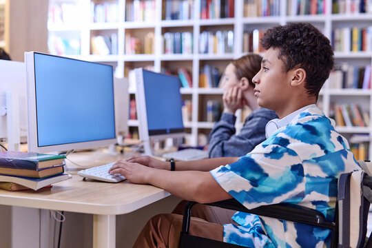 Side view portrait of Middle Eastern teenage boy using computer in school library and doing research online