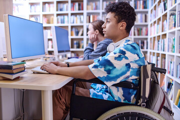 Side view portrait of Middle Eastern teenage boy with disability using computer in school library,...