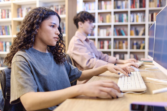 Side view portrait of Latin American teenage girl using computer in school library and doing research online