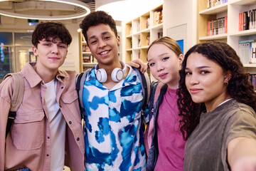 POV selfie photo of multiethnic group of students smiling at camera in school library