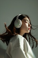 Beauty asian woman with her eyes closed enjoying the music wearing headphones in soft and plain grey background