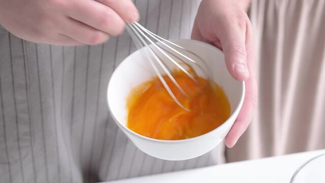 Whipping eggs in a ceramic bowl. Egg yolks and egg whites mixed with sugar. slow motion