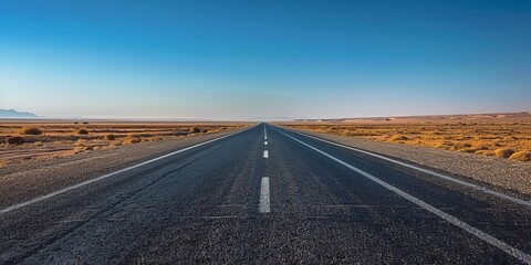 Wide-angle view of a long, deserted highway stretching under a clear blue sky, embodying a sense of freedom and travel