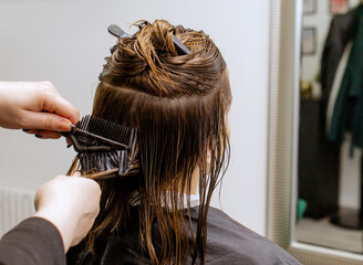 Fototapeta premium Woman professional hairdresser doing hair styling to client in beauty salon, applies balm to strengthen hair, stylist doing hair care procedures