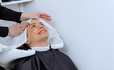 Woman professional hairdresser washing hair in a beauty salon, doing hair styling to client in...