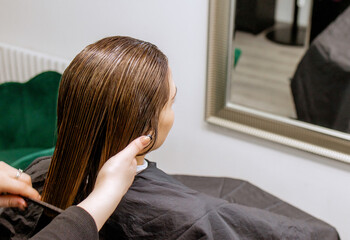 Woman professional hairdresser doing hair styling to client in beauty salon, applies balm to...