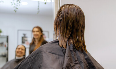 Woman professional hairdresser doing hair styling to client in beauty salon, applies balm to...