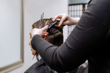 Woman professional hairdresser doing hair styling to client in beauty salon, cutting the ends of...