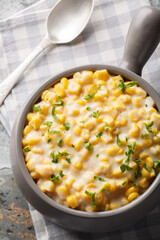 Thanksgiving side dish Creamed corn with butter, cheese, parsley closeup on the bowl on the table. Vertical top view from above