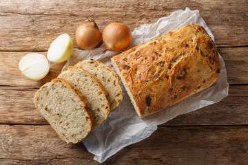 Yeast onion bread loaf with a crispy crust close-up on parchment on a wooden table. Horizontal top view from above