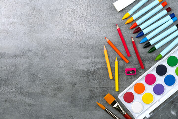 Watercolor paints set and paintbrush and colored pencils and crayons on stone texture background....