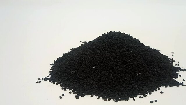 Pile of Black cumin seeds or black caraway seeds on white background isolated, moving from right to left, front view, close up, herbs and spices