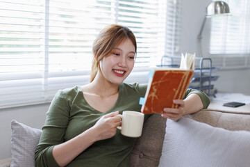 Young asian woman at home sitting on modern chair in front of window relaxing in her living room...