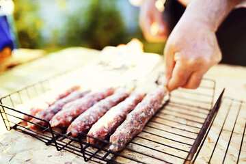 Selective focus. Cooking barbecue on the mangal in nature. Grilled tasty meet cooking on the party. Traditional Russian shashlik on a barbecue skewer on sunny forest.