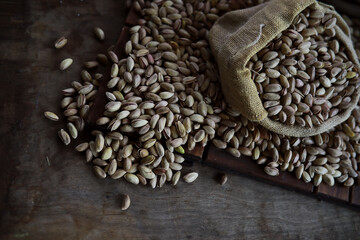 Pistachio nut in sack bag with mint green leaf on wooden table background.