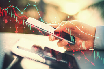 Side view of male hands using tablet and cellphone at desk with falling red forex chart and map on...