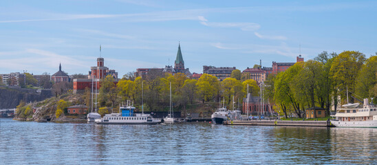 Small harbor ferry Djurgården arriving the island Skeppsholmen, the castle on the island Kastellholmen, the district Södermalm in the background, a sunny summer morning in Stockholm
