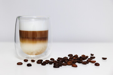 glass of fresh latte coffee with coffee beans on white table and copy space