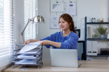 Young asian business woman working at home office with laptop and papers on desk