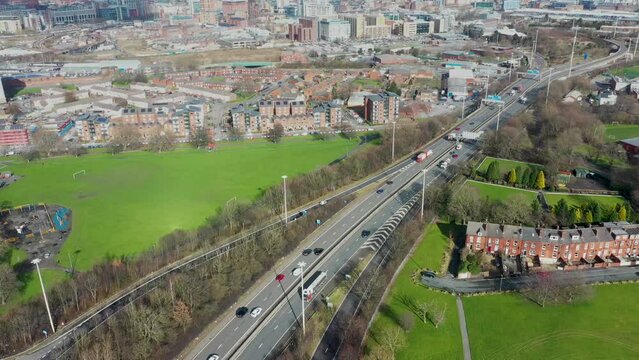 Aerial footage of the motorway in the UK known as the M62 showing traffic on the road on a beautiful sunny day in the spring time with the Leeds city centre in the background.