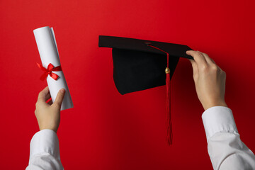 Graduate hat with diploma on red background.