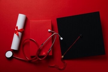 Graduate hat with diploma and stethoscope, on red background.