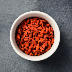 Close up of red dried goji berries in a bowl. On a dark concrete background.