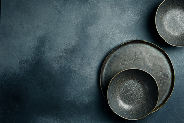 A set of dark ceramic bowls and plates. Close up on gray concrete background. Free space for text.