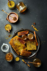 Honey background. Assortment of honey, honeycombs, pollen on a metal tray. On a black stone...