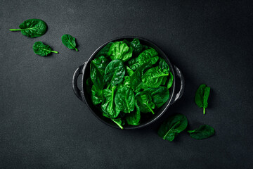 Spinach leaves in a black stone plate on a dark background. Top view.