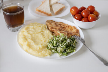 Tea in a glass and pickled tomatoes in a white plate and slices white bread. Tasty breakfast or lunch with mashed potatoes, chicken chop with salad -  green onion and green young cabbage.
