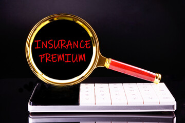 Financial concept. INSURANCE PREMIUM word appeared through a magnifying glass on a black background standing on a calculator