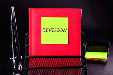 Conceptual revision symbol. REVISION word written on a yellow sticker on a red notepad in front of a black background. A place to copy
