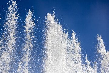 Liquid spraying from fountain against electric blue sky in natural landscape