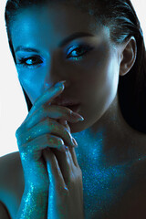 Mysterious womans face partially lit in a striking blue tone, her skin adorned with sparkling...